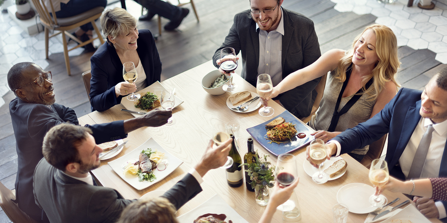 collegues in business attire sit at a restraunt table smiling and raising glasses in a toast