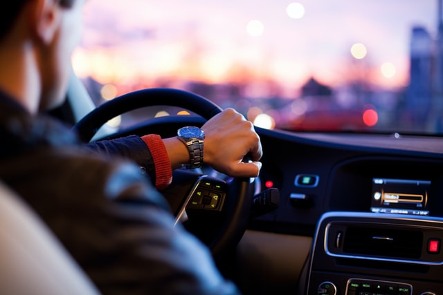 photo: over the shoulder shot of man driving car at dusk with dashboard illuminated