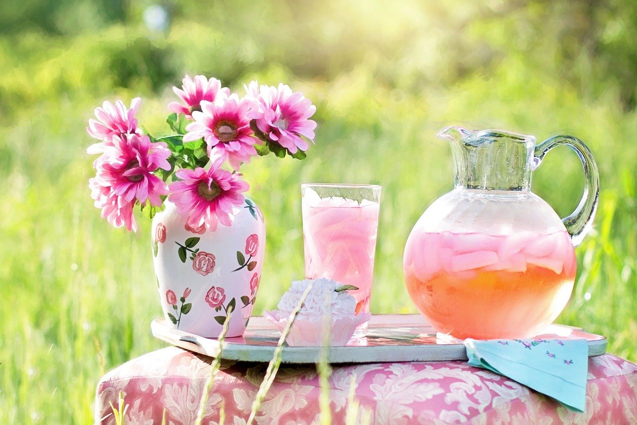 pitcher of strawberry lemonade sitting on a pink table in a grassy meadow