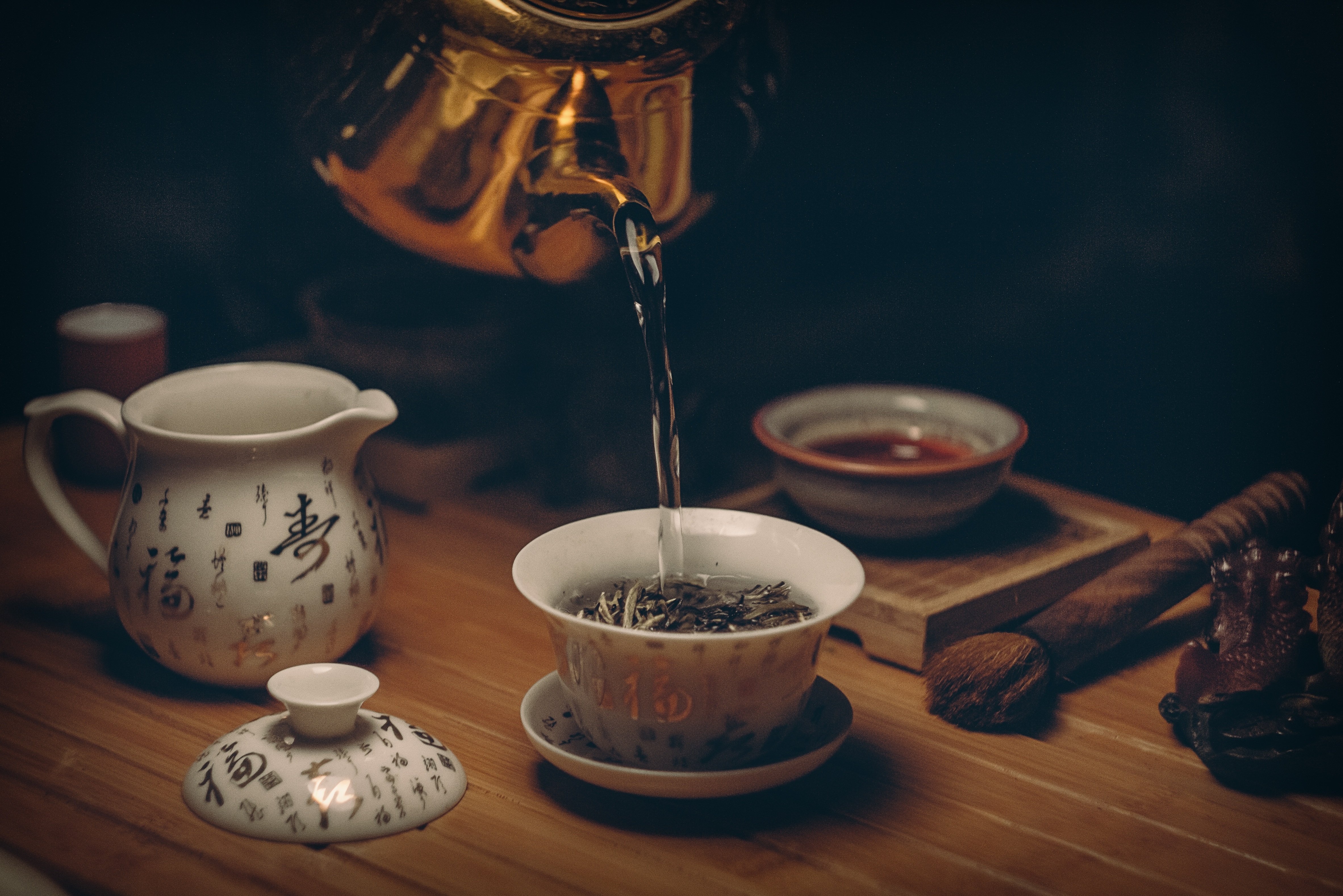golden kettle pouring hot water into a white teacup atop a wooden table