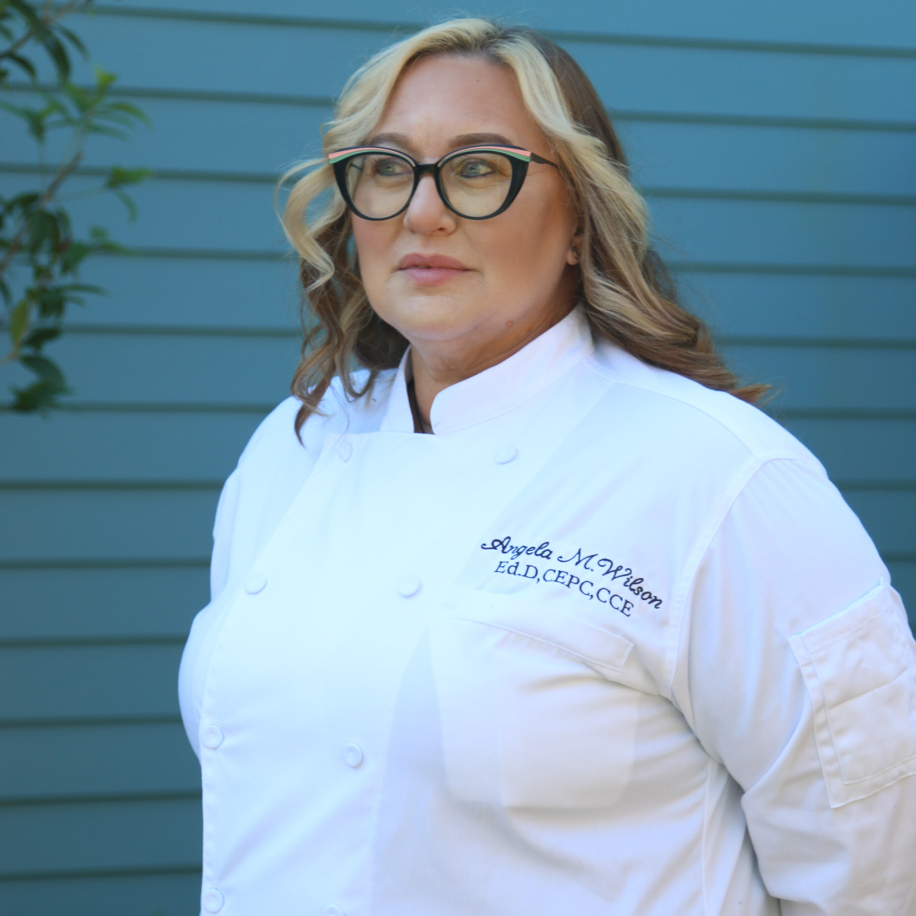 Blonde woman with glasses in chef's coat.
