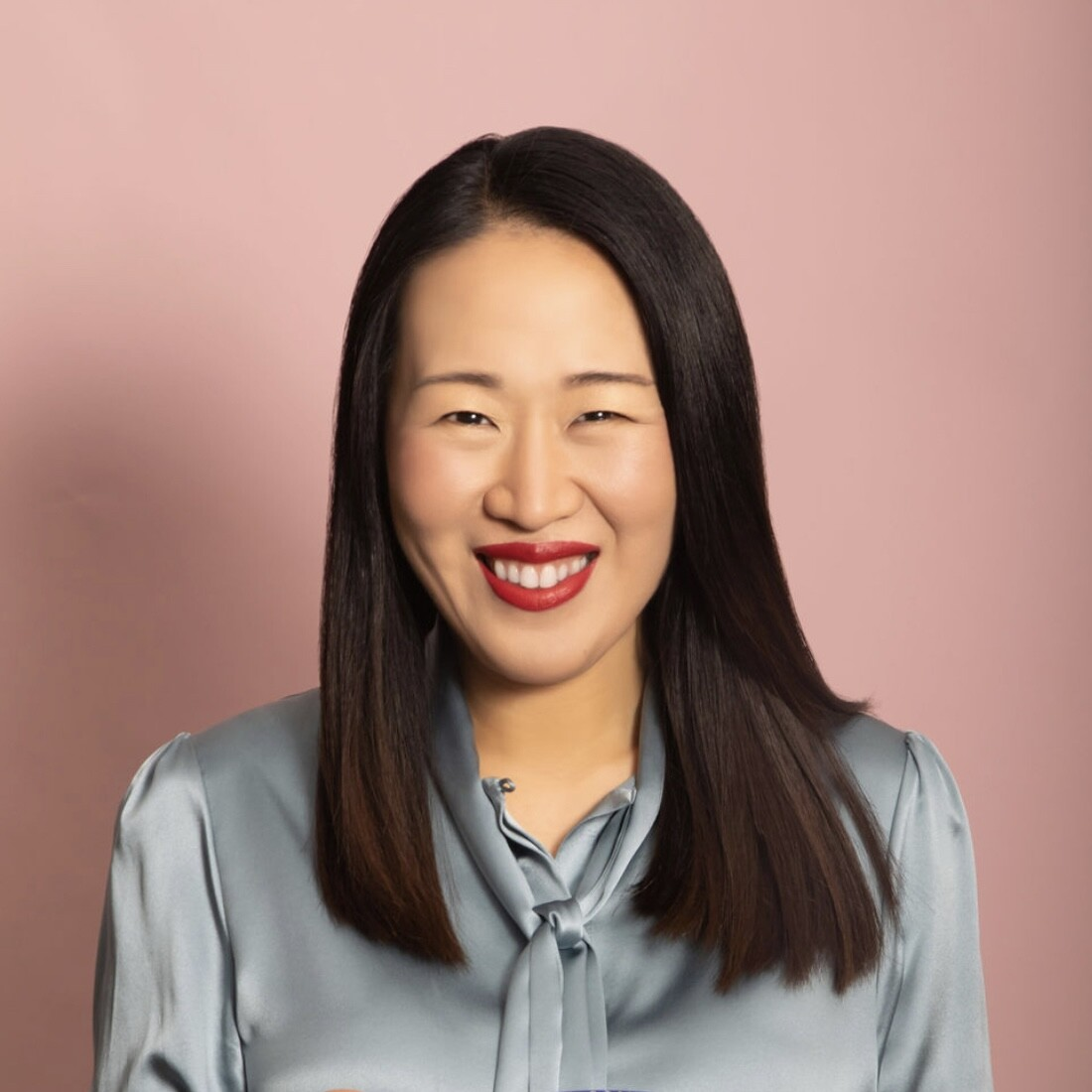 Woman smiles warmly looking straight into camera she has dark hair and a silver shirt