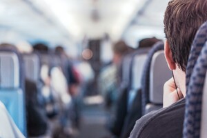 man wearing earphones in an aisle seat on a narrow-body jet looking toward the cockpit