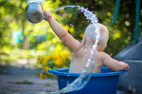 photo: baby in basin outside splashing with a cup