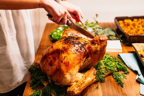 photo: knife carving a perfectly browned turkey sitting on a cutting board with herbs