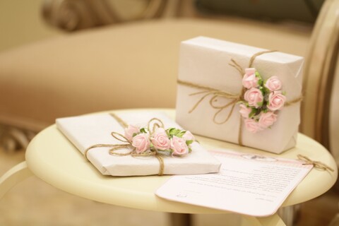 photo of two wedding gifts wrapped in white paper and twine with pink roses on a small table