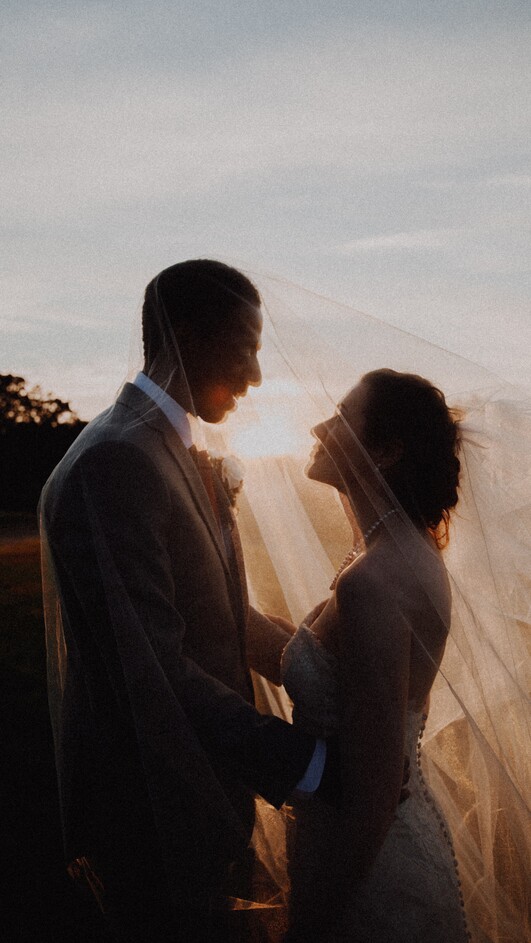 photo of a bride and groom under a veil at sunset