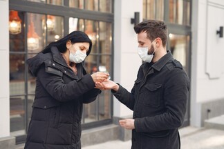 masked woman putting hand sanitizer in a masked man's hand