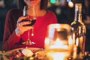 close up of intimate table setting with a woman in a red top holding a red wine glass