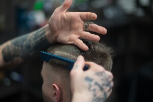 man getting a hard part haircut from a tattooed barber