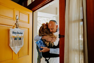 relatives hugging one another at the front door, with holiday decorations on the door and gifts in hand