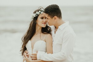 bride and groom in informal wedding attire embracing one another on a beach