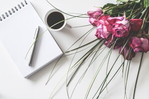 pen, pad of paper, cup of coffee, and a bouquet of flowers sitting on a white table