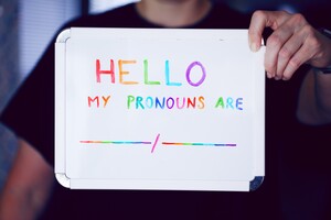 person holding a sign introducing themselves and their pronouns in multi-colored ink