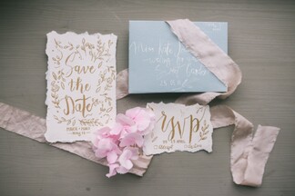 wedding invitations with pink ribbons on top of a light wooden table