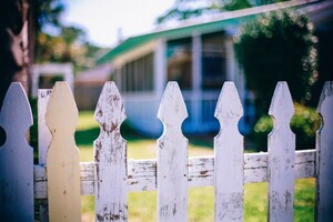 worn white picket fence with white and green home in background