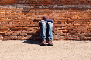 discouraged child sitting against a brick wall with his head down