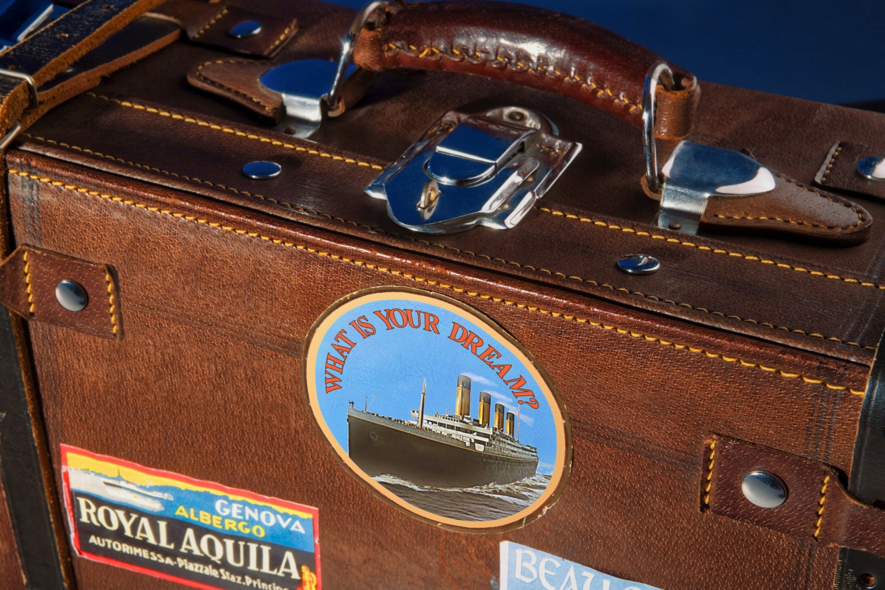 Brown leather suitcase with stickers on it. This is a close up so you cannot see the entire suitcase