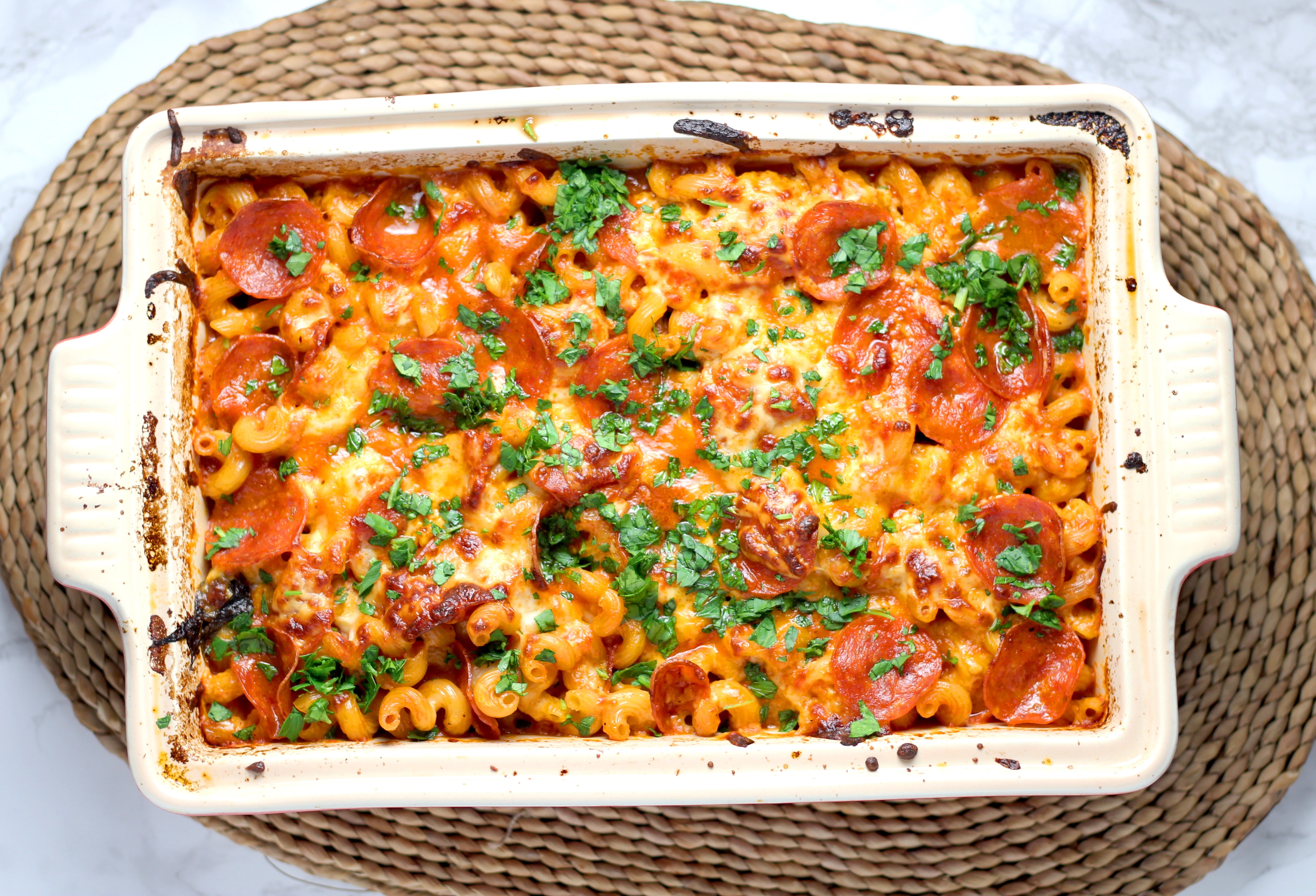 Macaroni and pepperoni casserole with basil sprinkled on top sits in a cream colored baking dish