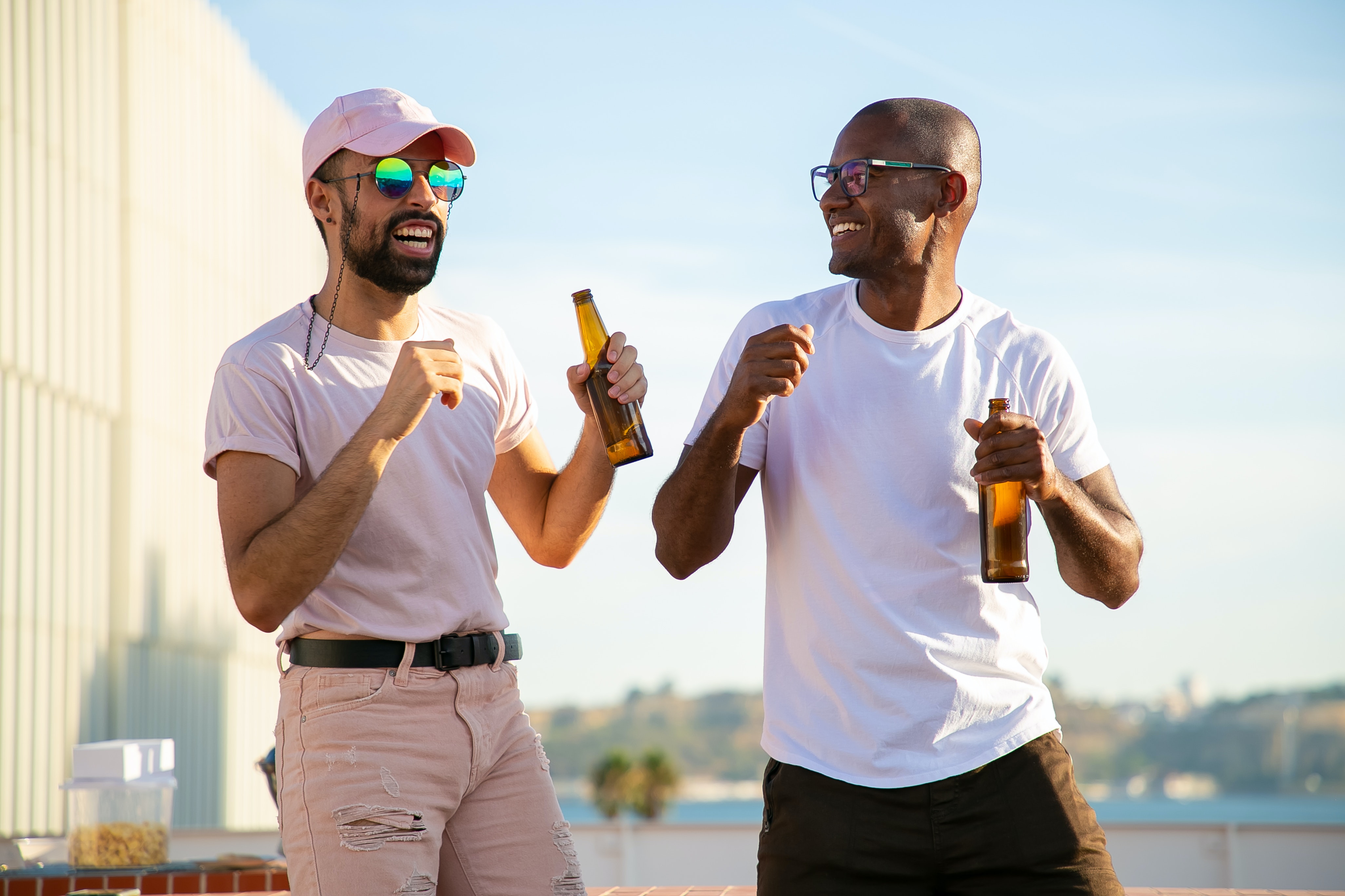 two men on a rooftop in the sun laughing and enjoying beers and snacks together