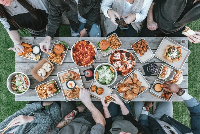 photo: shot from above a crowded table covered with different orders and eight people sitting arround eating