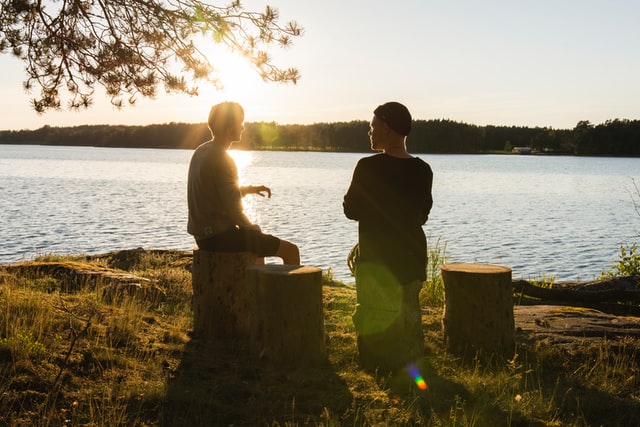 photo: two men sit by a lake talking at sunset