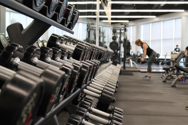 photo: weights nicely lined up on a rack at the gym with woman lifting in the background