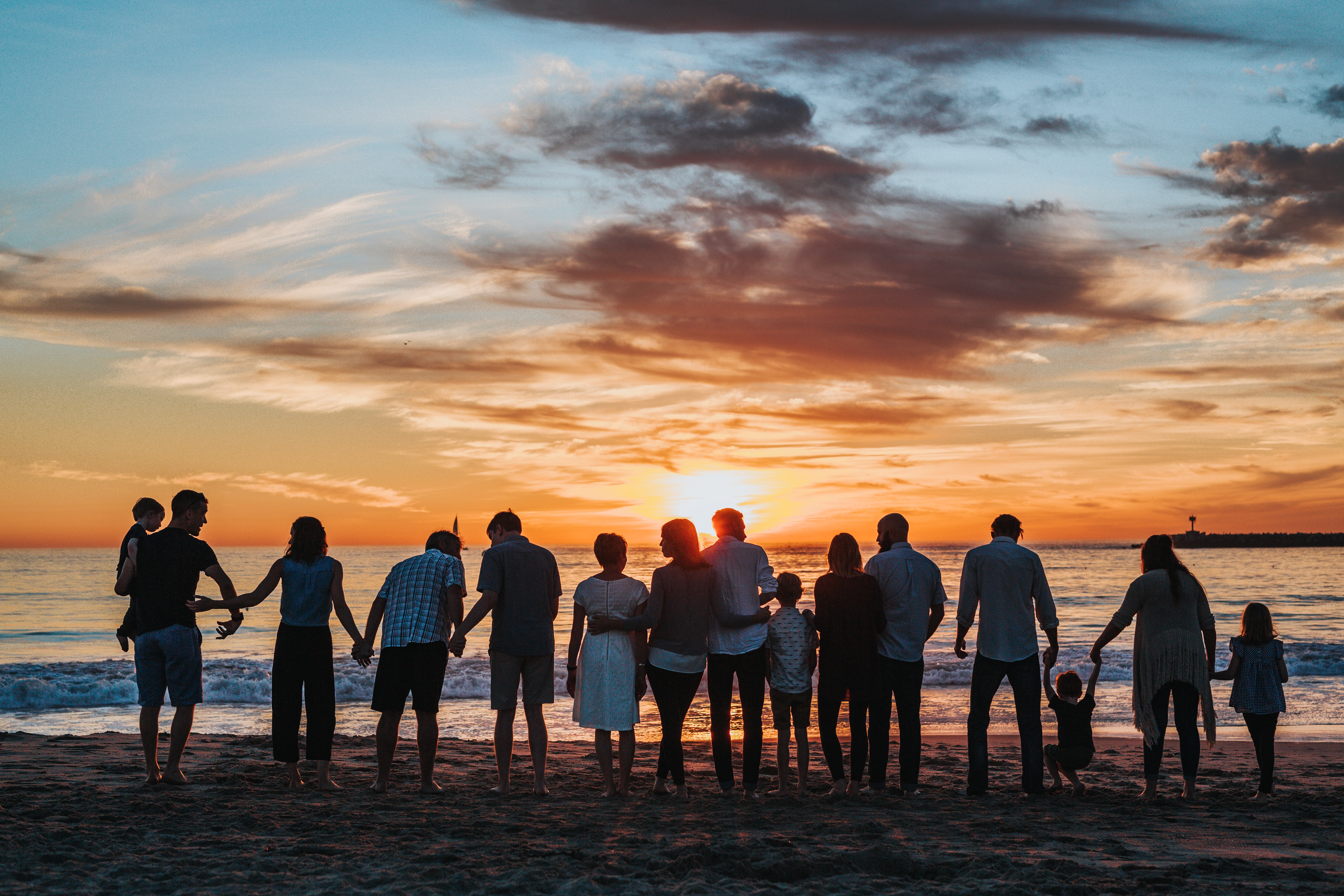 photo: big family stands in a line along the beach at sunset