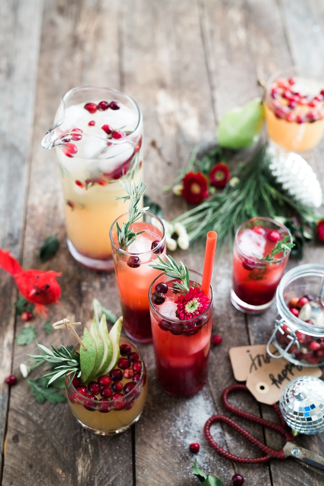 photo: festive mixed drinks with herbs and cranberries on a table with decorations, tags, and scissors.