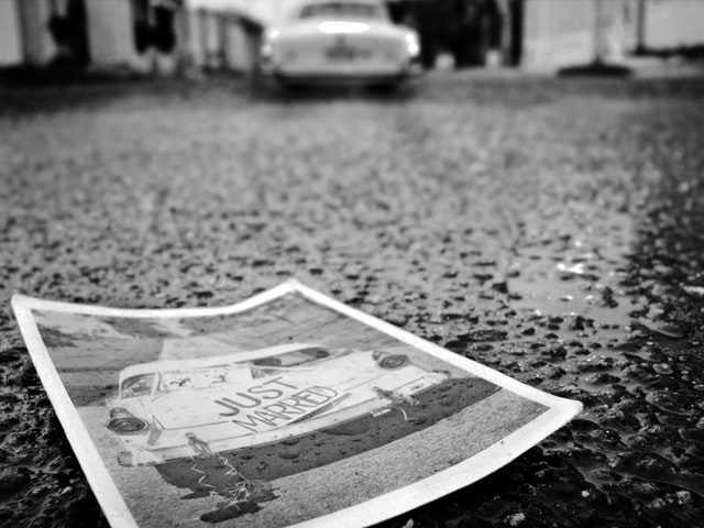photo: black and white photo of just married sign on a car sits on the road in the rain