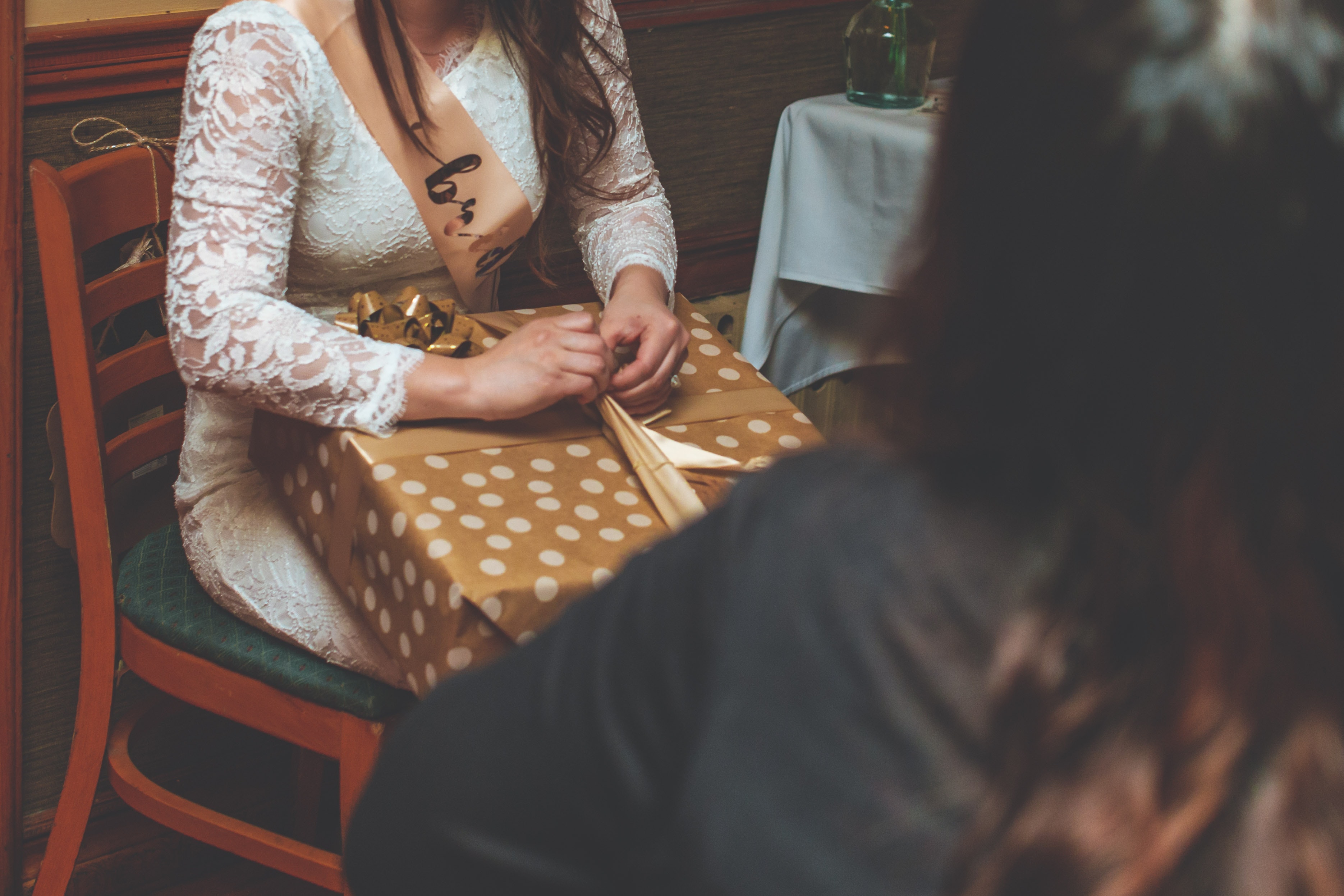 bride in white dress sitting on a wooden chair opening gifts
