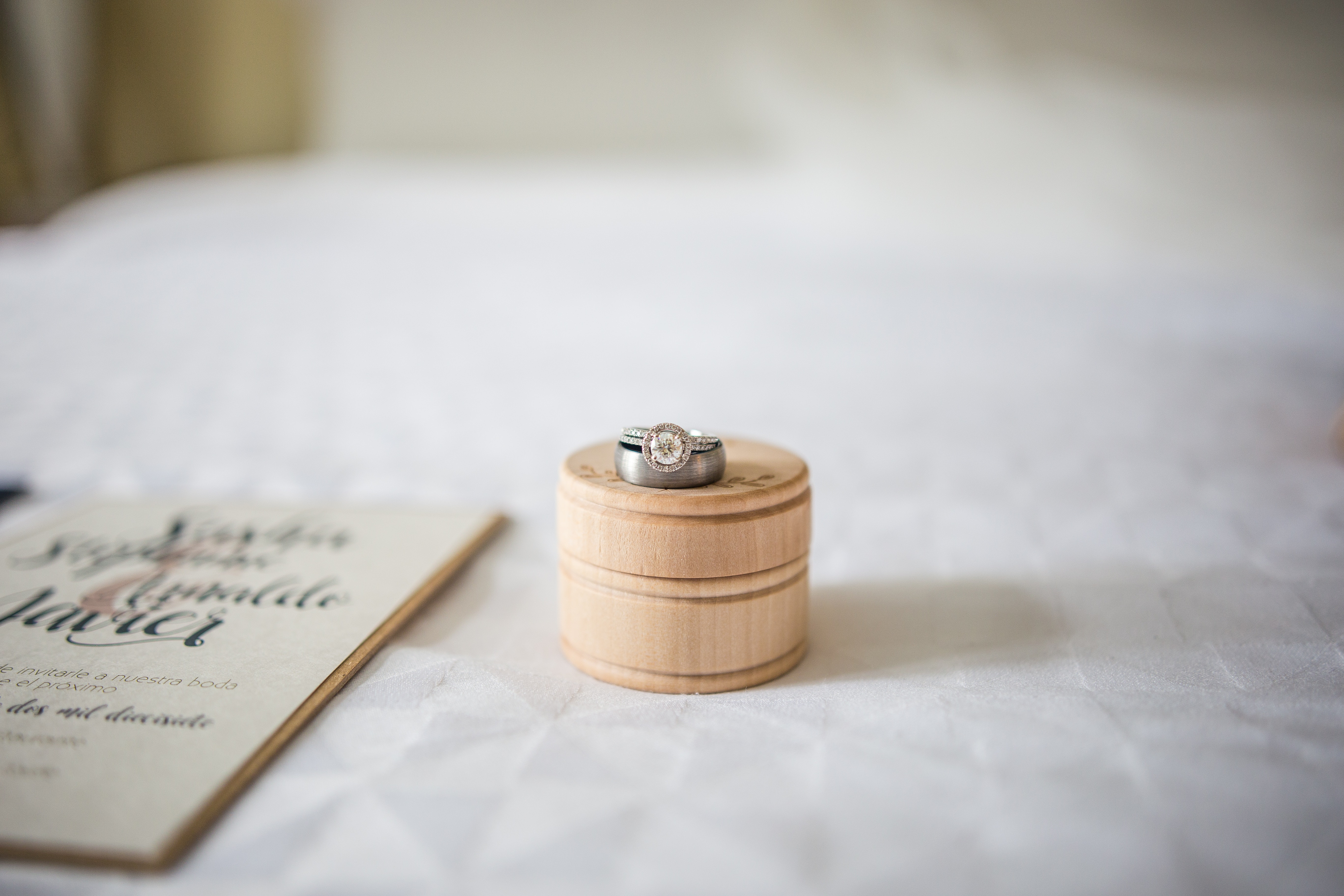 wedding rings on top of a white cloth table with a wedding invitation next to them