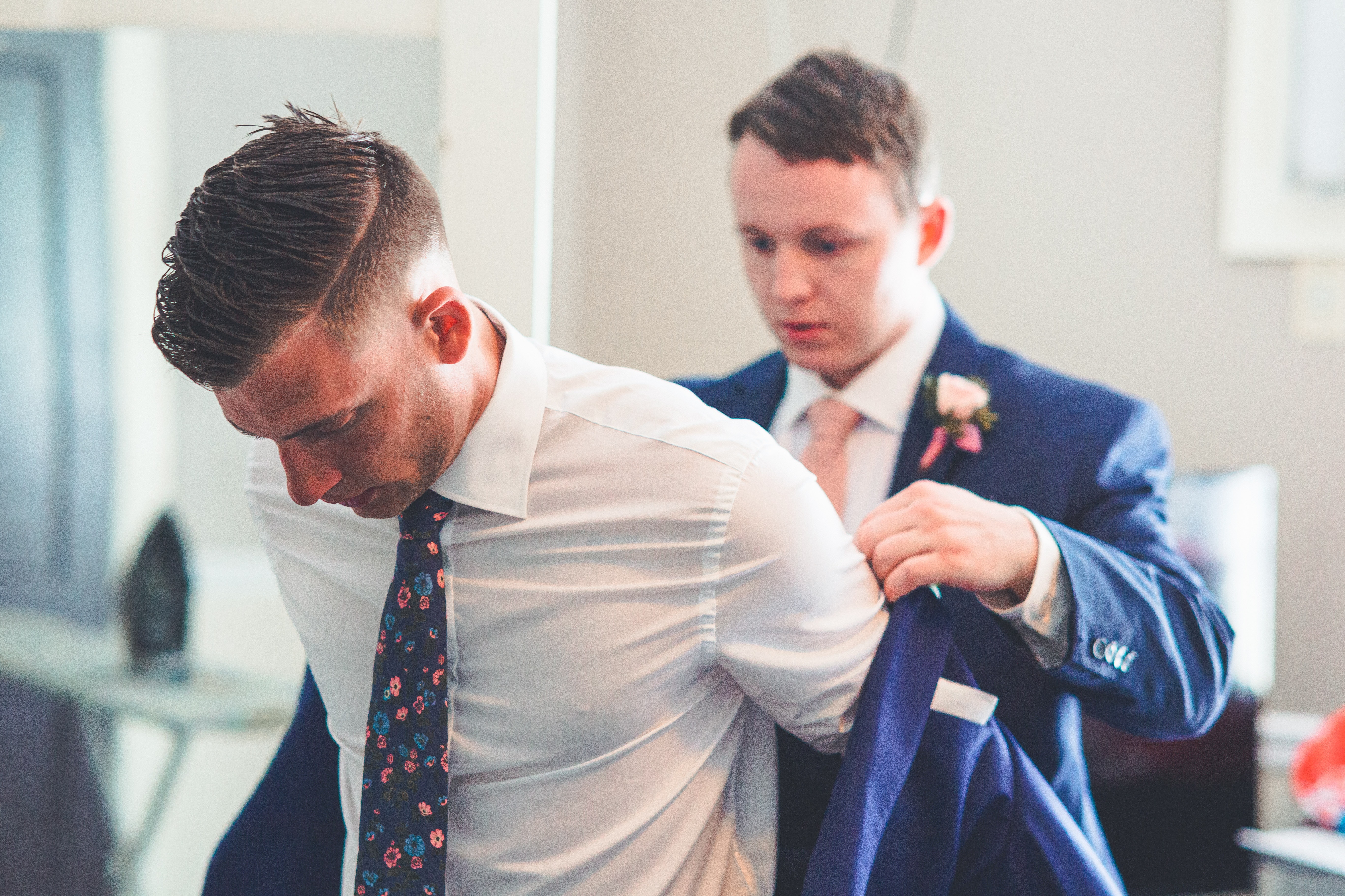 groom putting on his formal coat with the help of a groomsman