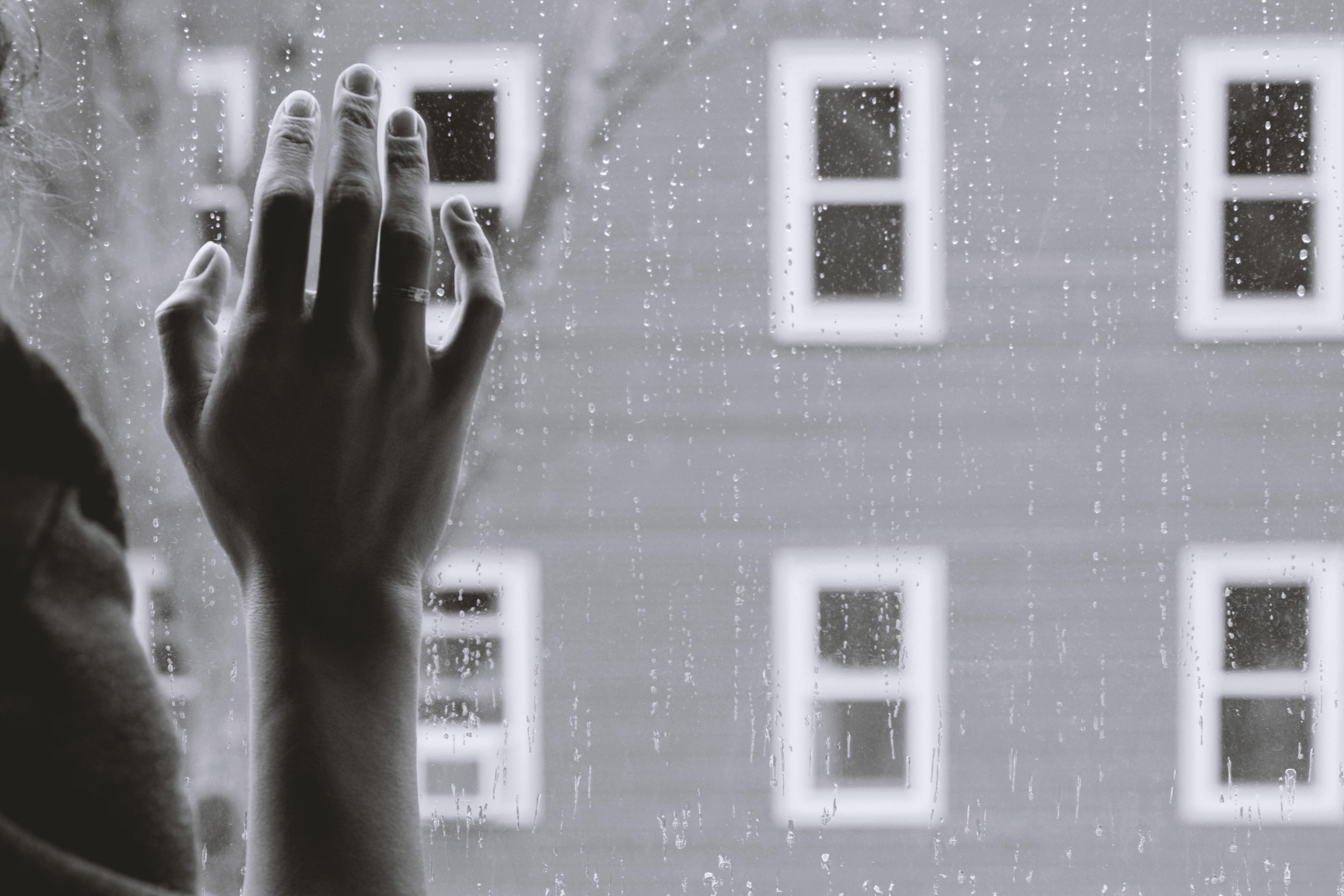 person with their right hand on a window, with rain drops trickling down