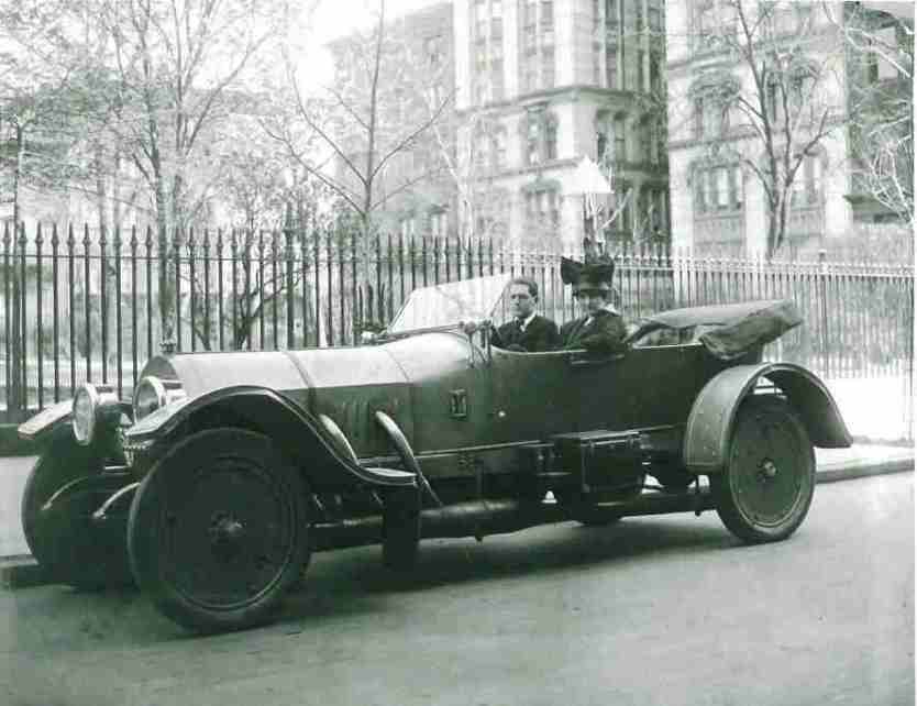 Picture of young Emily Post sitting in a large mercedes automobile wearing a hat with a large bow in front of a NY townhouse, 1916