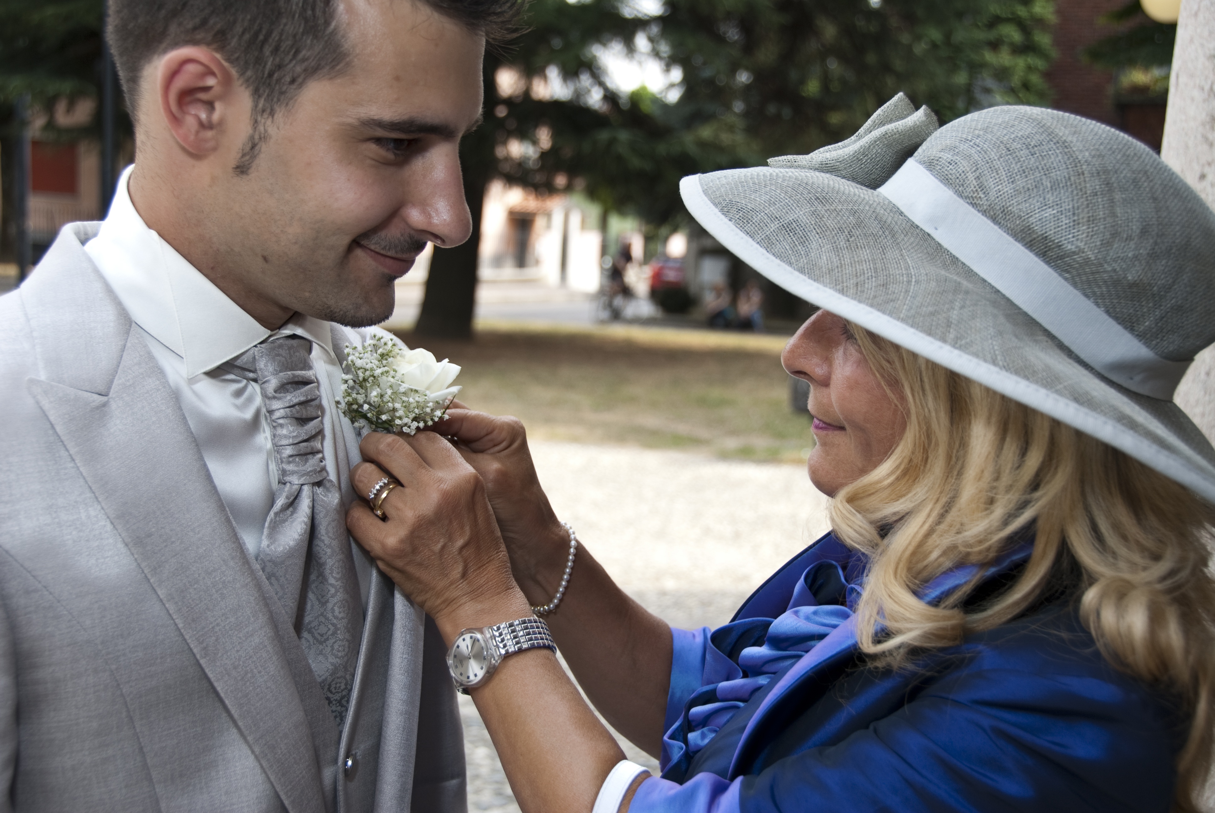A mother fixing the boutonniere on her son's wedding suit.  From https://emilypost.com/advice/wedding-attire-tips-for-the-moms
