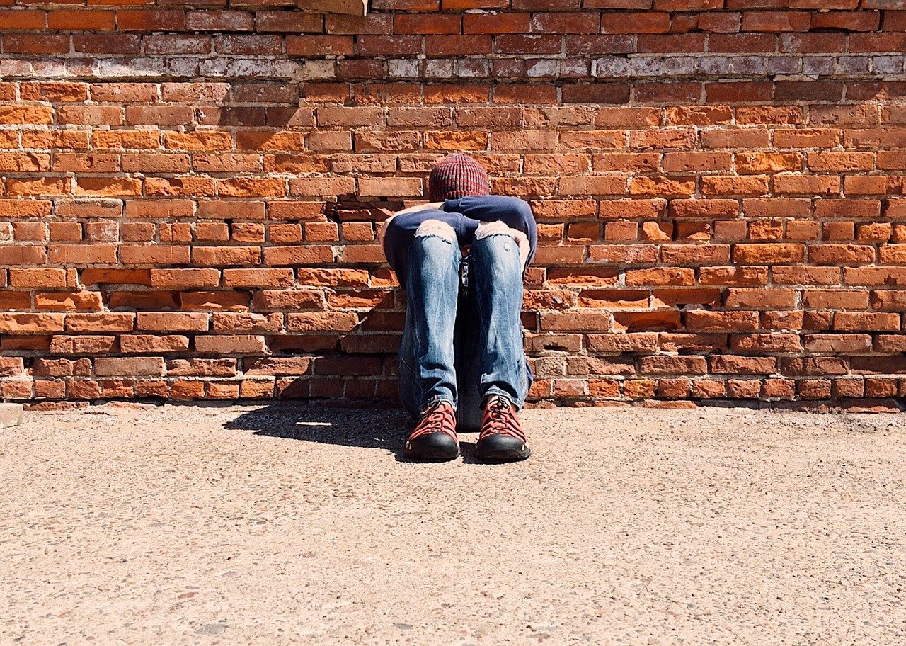 discouraged child sitting against a brick wall with his head down